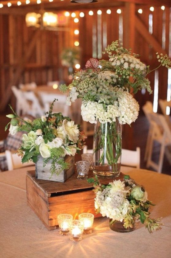 a barn wedding centerpiece of candles, neutral blooms and greenery plus succulents and a wooden box