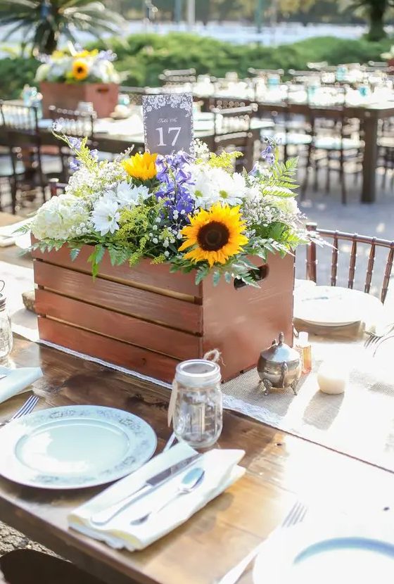a beautiful rustic wedding centerpiece in a crate, with sunflowers, white hydrangeas, purple blooms, baby's breath and fern is a gorgeous solution