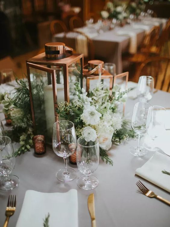 a beautiful wedding centerpiece of candle lanterns and greenery and white blooms on the table is lovely