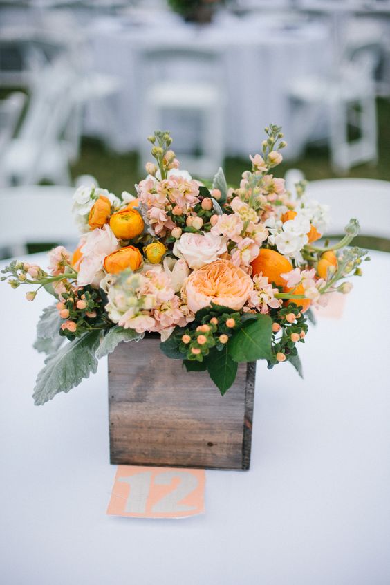 a bold summer wedding centerpiece of a wooden box with blush and orange blooms, berries and leaves