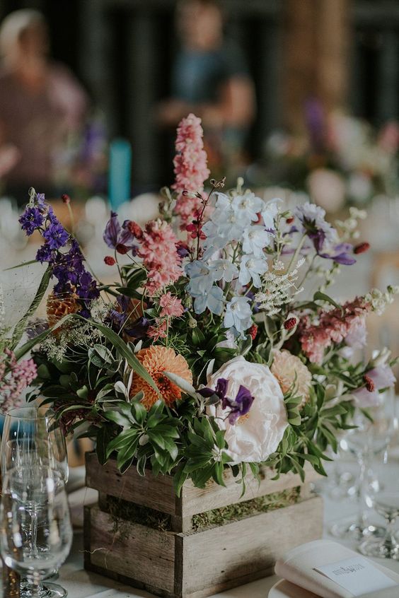 a bold wedding centerpiece of a crate with greenery, pastel and white blooms is a catchy and cool idea for decorating