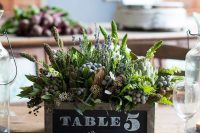 a catchy textural wedding centerpiece of a wooden box with greenery, leaves, berries and some wildflowers