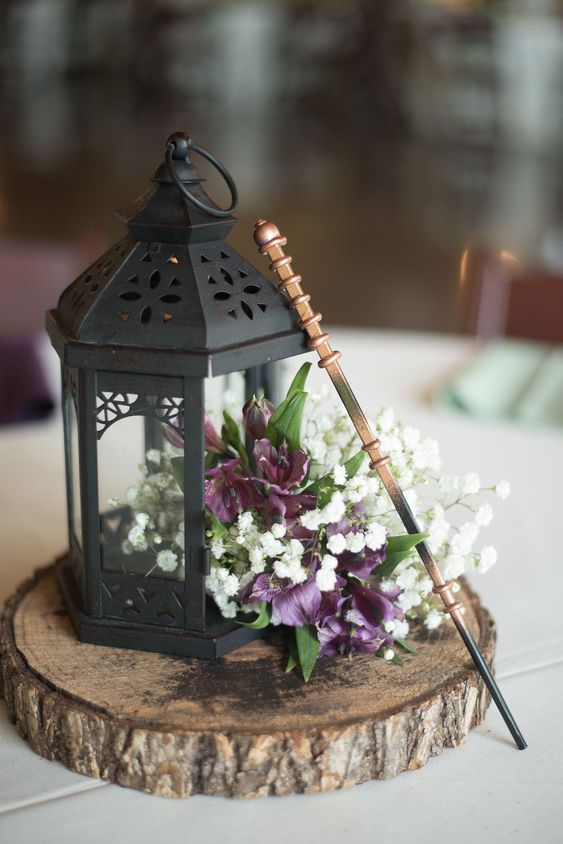 a catchy wedding centerpiece of a tree slice, a black lantern with purple and white blooms and a wand for a fairy-tale wedding