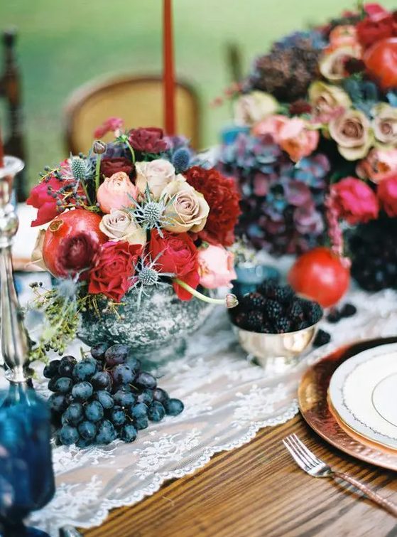 A chic jewel tone wedding centerpiece with red and blush roses, thistles and pomegranates in a silver bowl