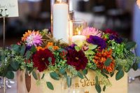 a colorful wedding centerpiece of a crate with super bold blooms and greenery and candles in tall glasses is cool