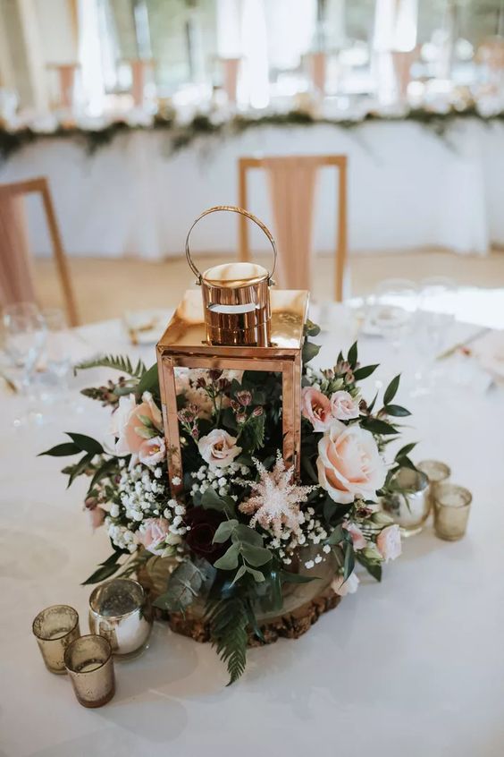 a delicate rustic wedding centerpiece of a tree slice, a lantern with blush blooms and greenery is amazing