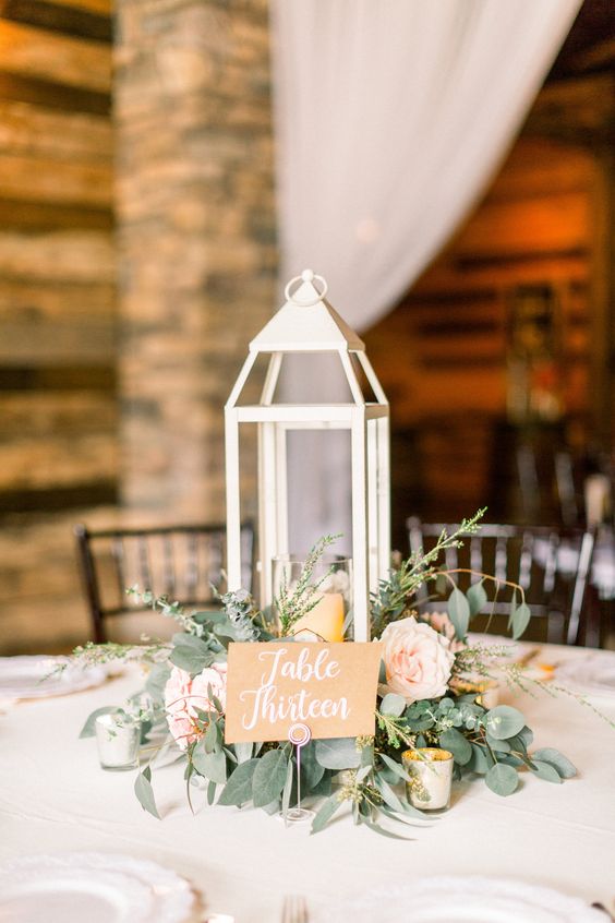 a delicate wedding centerpiece of greenery, blush blooms, a candle lantern is a cool and catchy idea for a rustic wedding