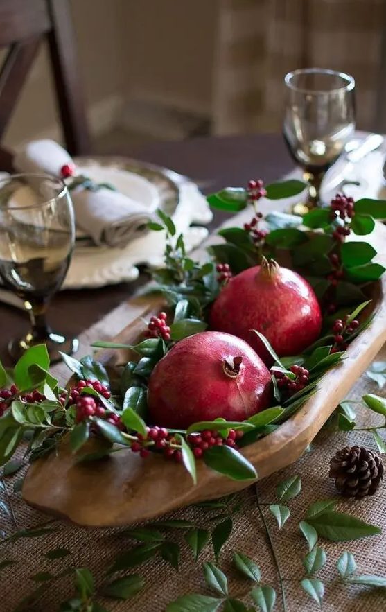 a fall wedding centerpiece of a wooden bowl, greenery, berries and pomegranates is a lovely idea for a fall rustic wedding