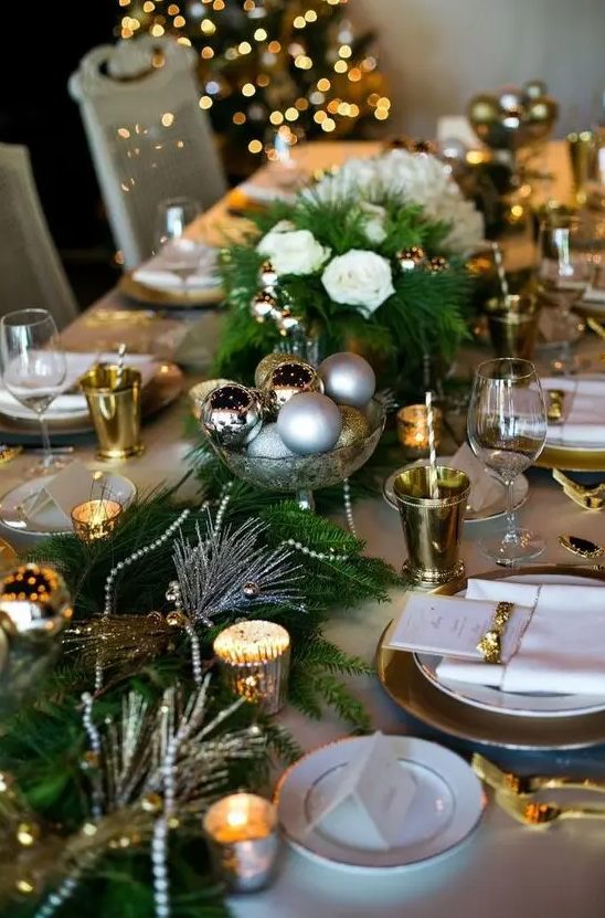 a festive table runner with evergreens, candles, beads and Christmas ornaments in a metallic bowl