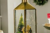 a lantern Christmas terrarium with faux snow, a gold deer, bottle brush trees and some greenery is a chic solution