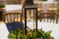 a modern wedding centerpiece of a candle lantern with lights and greenery is a super cool idea for many weddings