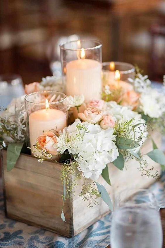 a neutral wedding centerpiece of a wooden box with neutral and pastel blooms and pillar candles