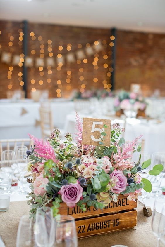a pretty spring or summer wedding centerpiece of a crate with greenery, blush and pink blooms and thistles