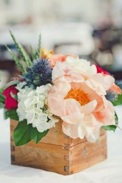 a pretty spring wedding centerpiece of a wooden box with pastel, white and bold blooms and thistles
