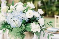 a pretty textured wedding centerpiece of white roses and blue hydrangeas, leaves and fern in a brass bowl is wow