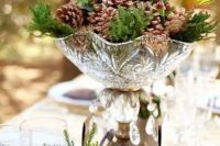 a pretty winter wedding centerpiece of a crystal bowl with pinecones, berries and evergreens is a delicate and cool idea for a woodland wedding