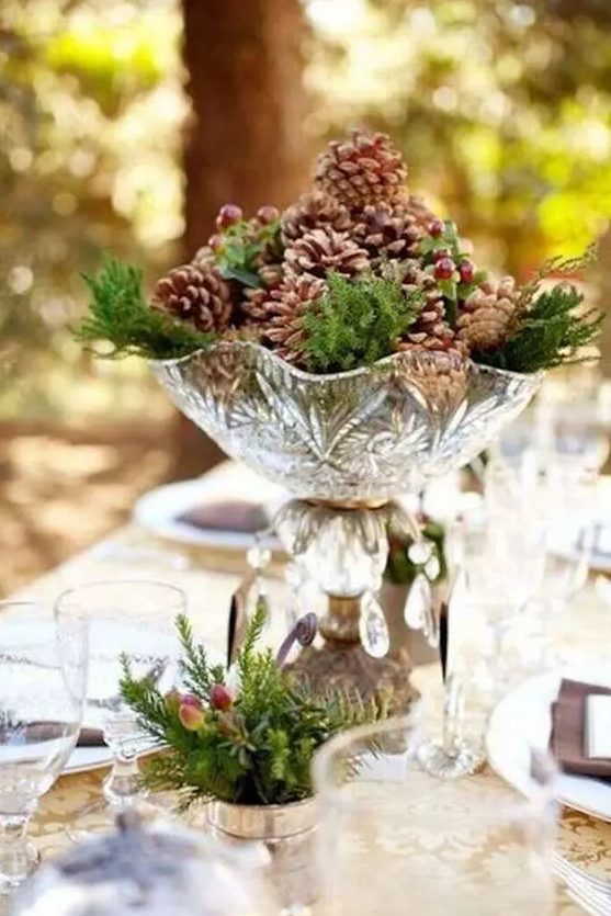 a pretty winter wedding centerpiece of a crystal bowl with pinecones, berries and evergreens is a delicate and cool idea for a woodland wedding