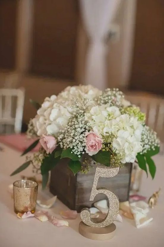 a reclaimed wooden box with baby's breath, hydrangeas and roses, a glitter table number for a rustic wedding centerpiece