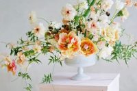 a refined summer wedding arrangement of light pink, peachy and yellow blooms and textural greenery