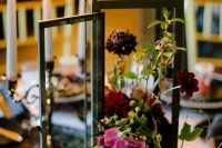 a refined wedding centerpiece of a candle lantern filled with dark blooms and greenery is amazing to style your wedding table