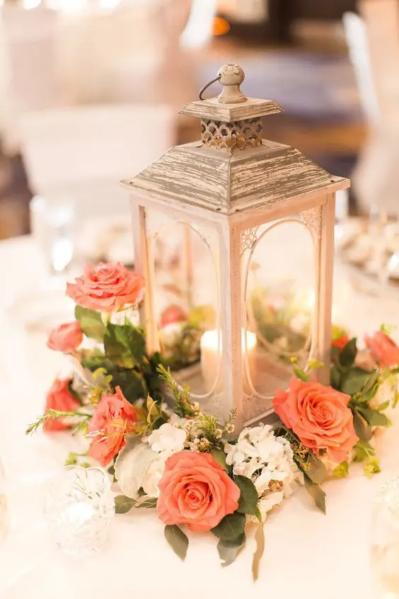 a refined wedding centerpiece of a lantern surrounded with coral and white blooms and greenery