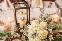 a refined winter wedding centerpiece of white hydrangeas, baby’s breath, pinecones, a candle lantern and greenery is a cool idea to go for