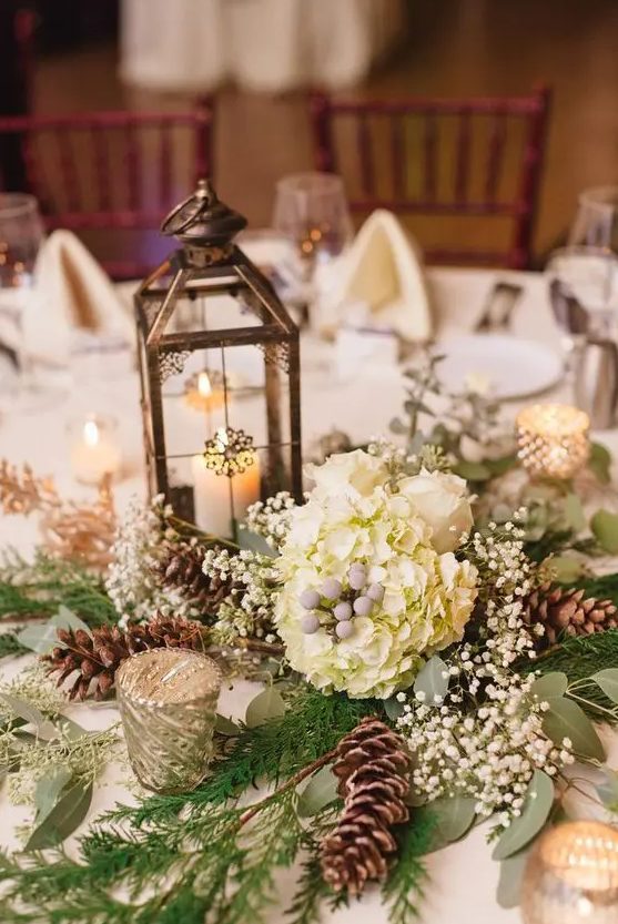 a refined winter wedding centerpiece of white hydrangeas, baby's breath, pinecones, a candle lantern and greenery is a cool idea to go for