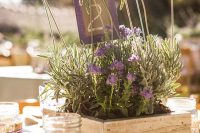 a relaxed Provence wedding centerpiece of a wooden box with greenery and purple blooms and a table number