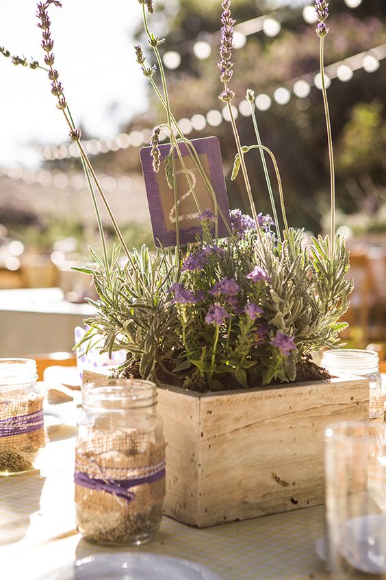 a relaxed Provence wedding centerpiece of a wooden box with greenery and purple blooms and a table number