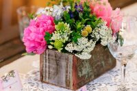 a rustic and colorful wedding centerpiece of a wooden box with bright blooms, greenery and some pastel flowers