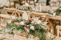 a rustic wedding centerpiece of a crate with greenery, neutral blooms and berries and a table name