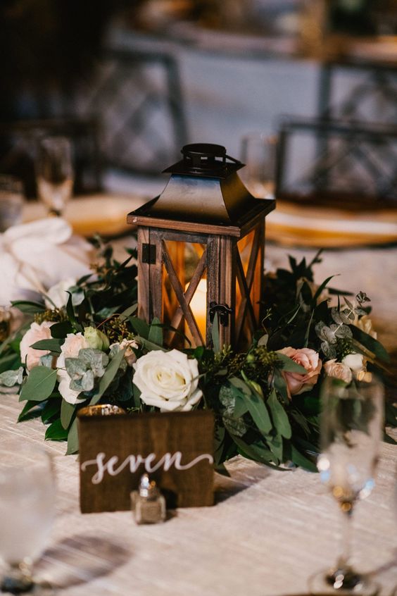 a rustic wedding centerpiece of a lantern, blush and white blooms and greenery is a cool and chic idea