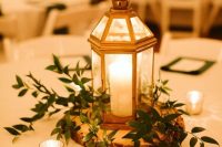 a rustic wedding centerpiece of a tree slice, greenery and a lantern is a cool and catchy decor idea for Christmas