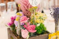 a rustic wedding centerpiece of a wooden box with greenery and bright blooms plus a table number is catchy and cool