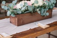 a rustic wedding centerpiece of a wooden box with greenery, white and pastel blooms is a cool solution