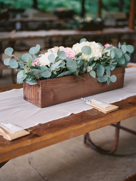 a rustic wedding centerpiece of a wooden box with greenery, white and pastel blooms is a cool solution