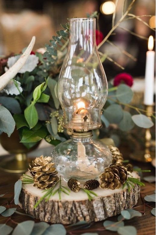 a rustic winter wedding decoration of a wood slice, a lantern and gilded pinecones plus greenery around