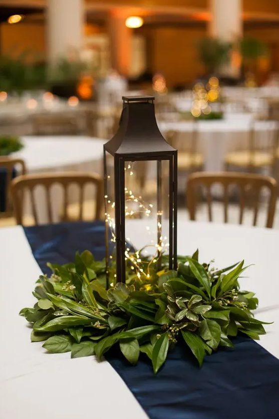 a simple and cozy Christmas wedding centerpiece with fresh greenery and a lantern filled with LEDs