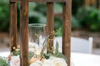 a simple and elegant wedding centerpiece of a wood frame with a candle and white and blush blooms and greenery for a rustic wedding