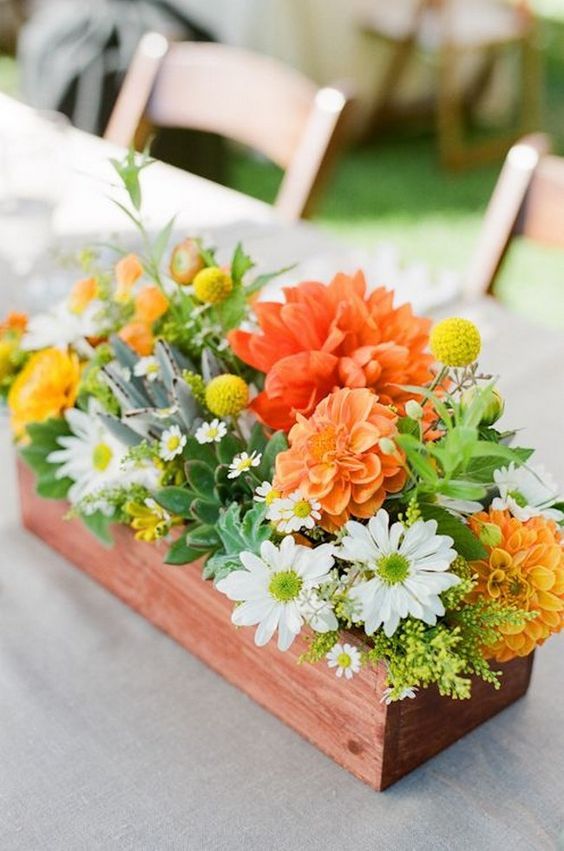 a summer wedding centerpiece in a box, with white, orange and yellow blooms, greenery and billy balls