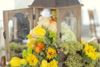 a vintage wedding centerpiece of a vintage candle lantern filled with sunflowers, yellow tulips, billy balls, white and blush roses and candles around