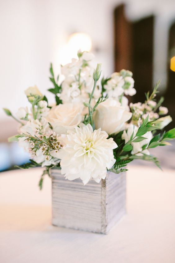 a white wedding centerpiece of a whitewashed box with white blooms and greenery is a catchy solution