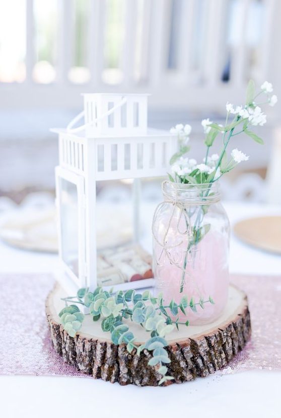 a wood slice, a white candle lantern with wine corks, a pink jar with some wildflowers and eucalyptus