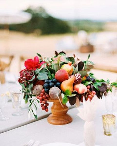 a wooden bowl with lots of fruit, berries, leaves and bright blooms is a lovely summer or fall wedding centerpiece