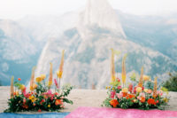 05 The ceremony space is decorated with orange, yellow, pink and red blooms and boho rugs