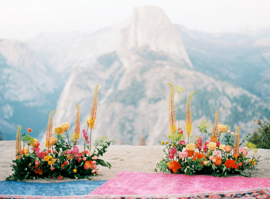 The ceremony space is decorated with orange, yellow, pink and red blooms and boho rugs