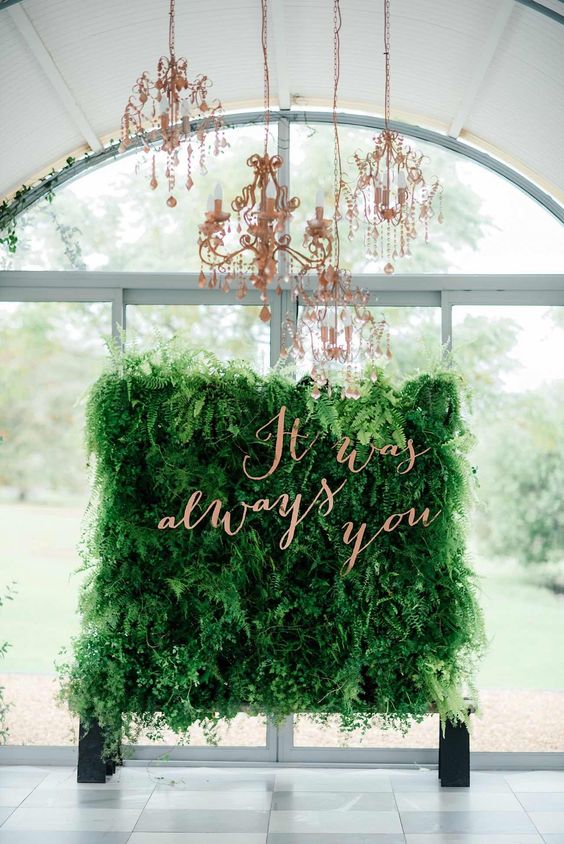 a lush fern wedding backdrop with a copper quote and copper chandeliers