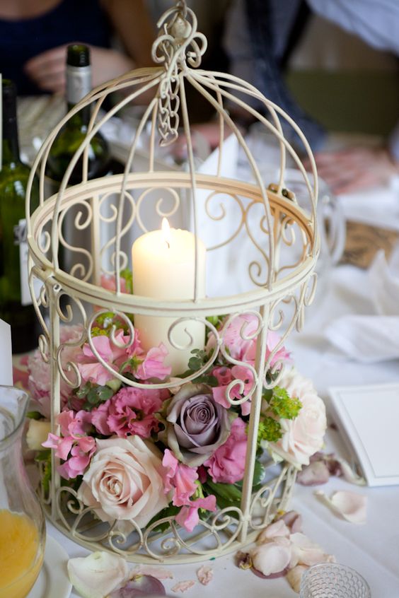 a white birdcage with lush pink blooms and a candle but be careful not to burn the flowers