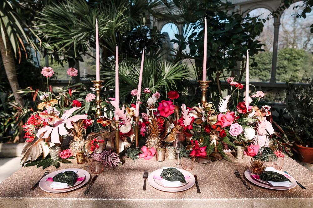The bold tablescape was done with pink hues, gilded pineapples and tropical leaves, pink candles added glam