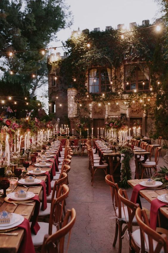 a wedding reception with burgundy touches and lots of lights in the backyard of a castle